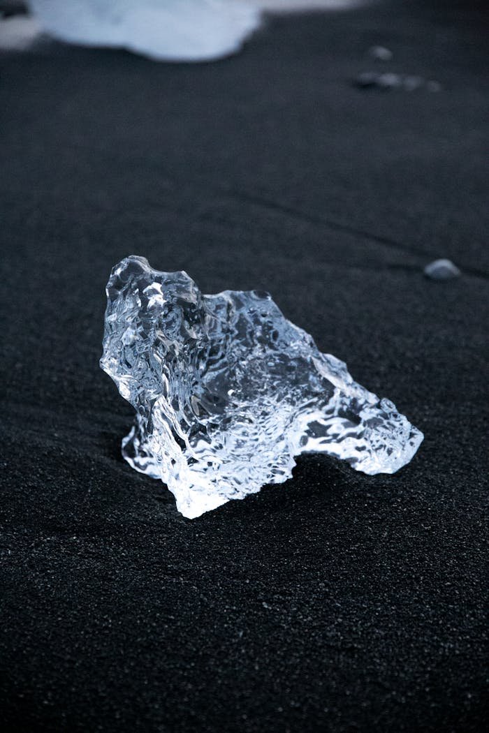 A clear ice fragment rests on the unique black sands of Diamond Beach in Iceland.